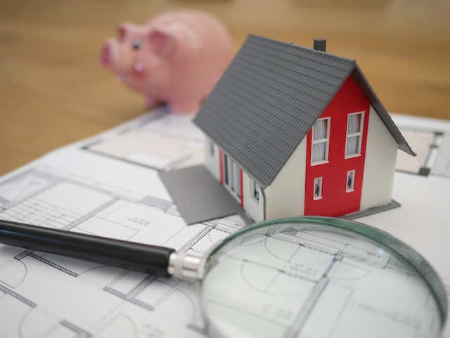 Une maison miniature sur un plan d'architecte avec une loupe et un petit cochon rose